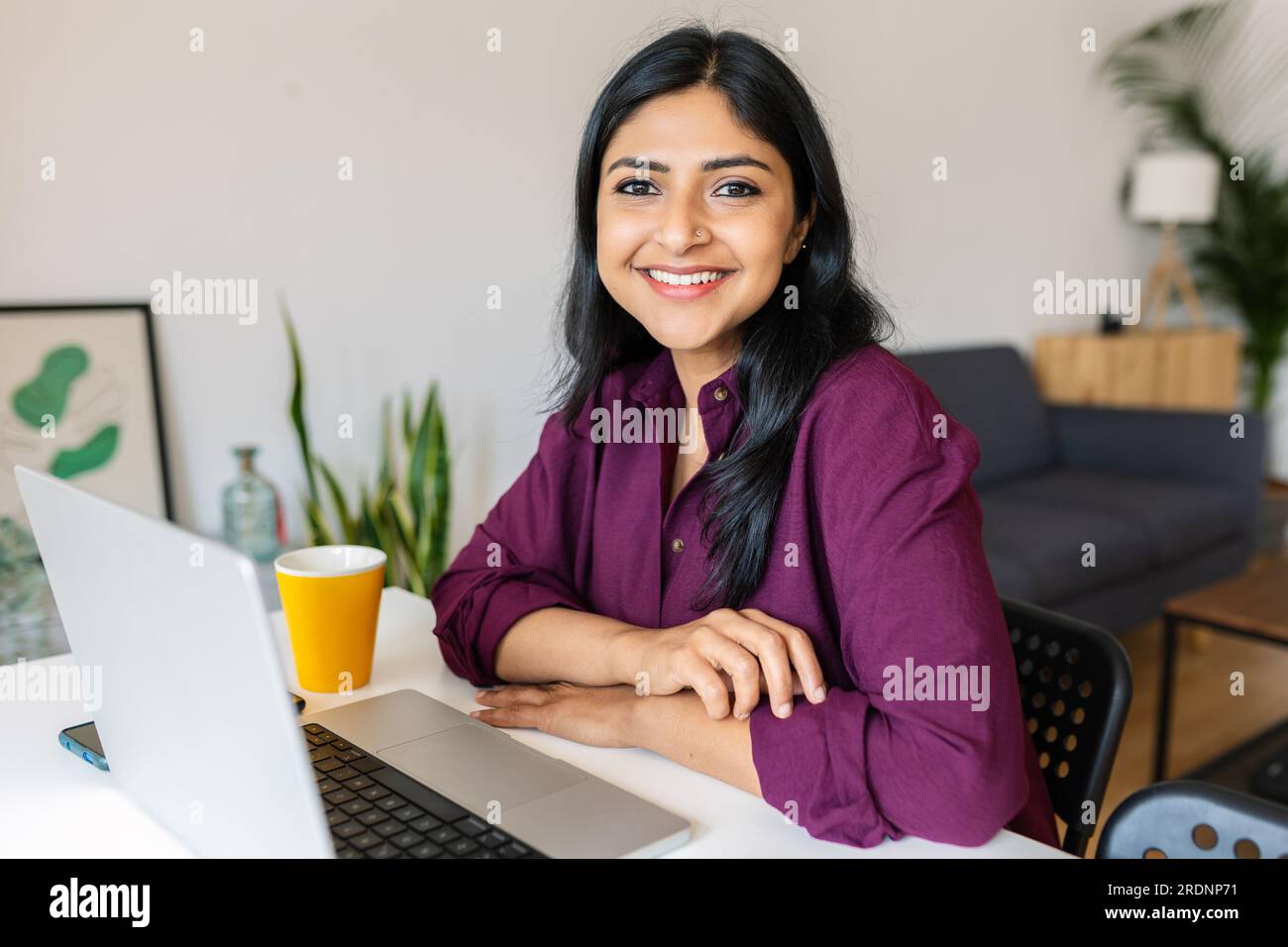 Young indian woman smile at camera working with laptop at home Stock Photo