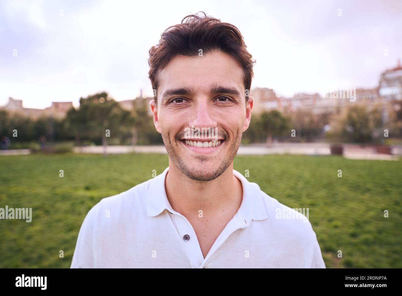 Portrait of attractive smiling young man looking at camera in park ...