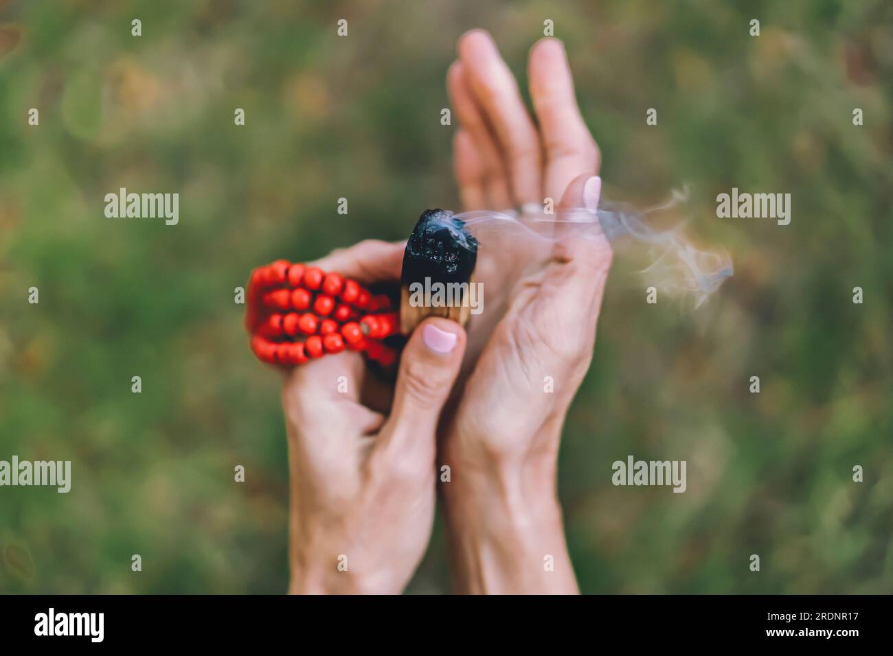 Top angle view of a palo santo or a holy sacred tree stick, burning with aroma smoke held by woman's hands over nature background Stock Photo