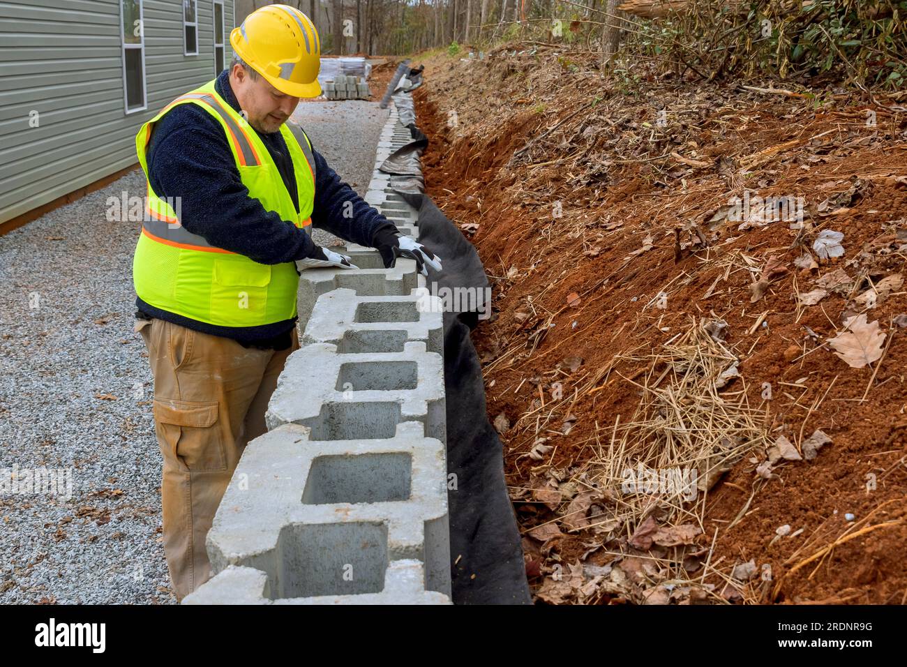 Construction worker is mounting retaining wall using concrete blocks to