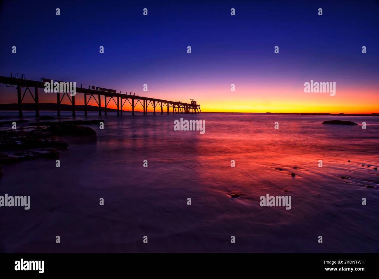 Pink scenic sunrise over Pacific ocean horizon by historic jetty on MIddle Camp beach in Australia. Stock Photo
