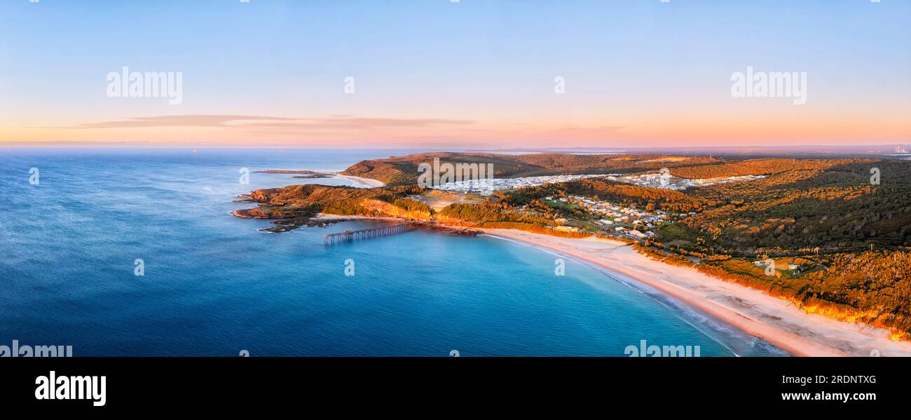 Scenic aerial panorama of Cathrenie Hill bay Middle Camp beach with historic jetty at sunrise. Stock Photo