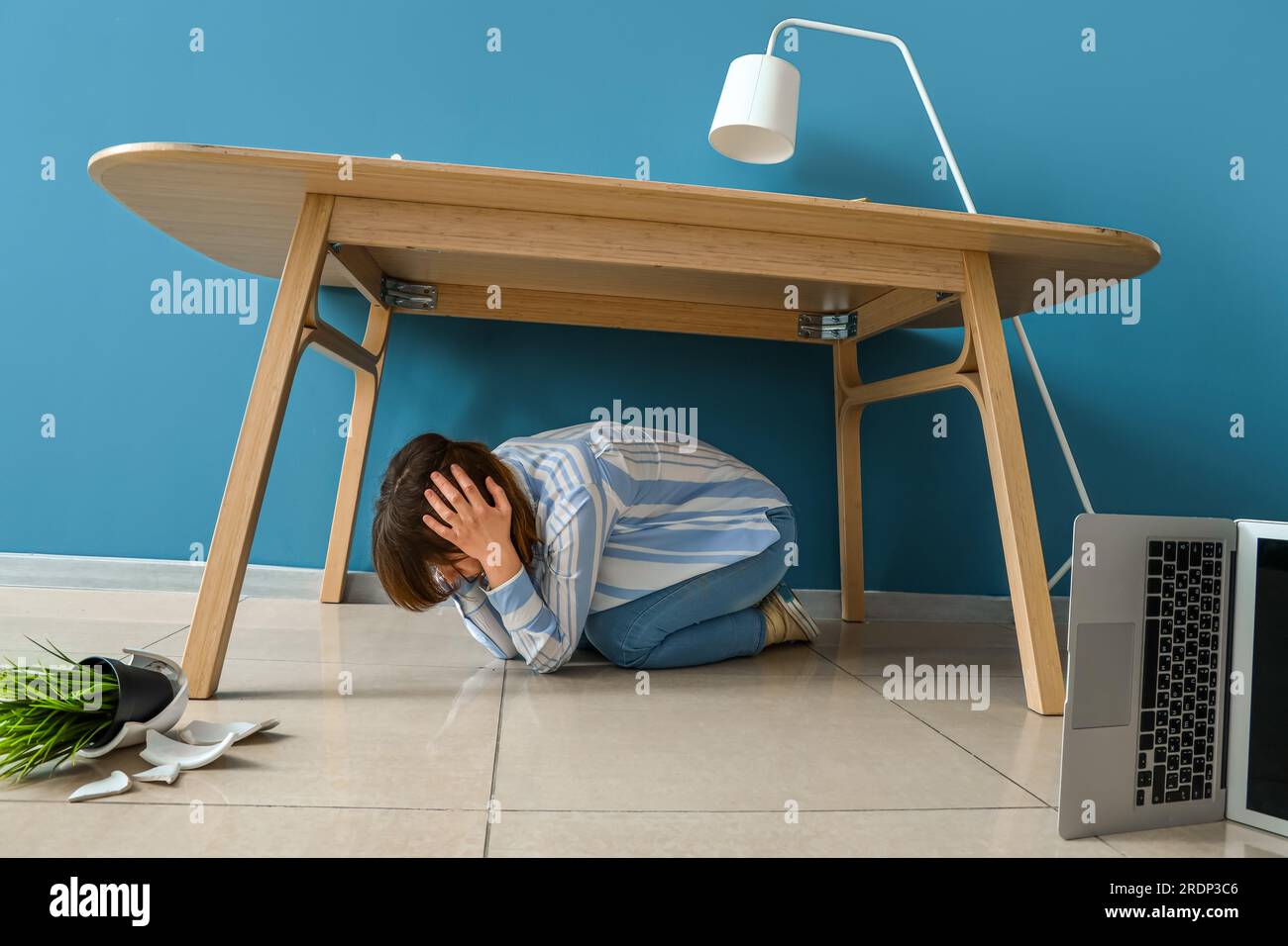 Young woman hiding under table during earthquake in office Stock Photo