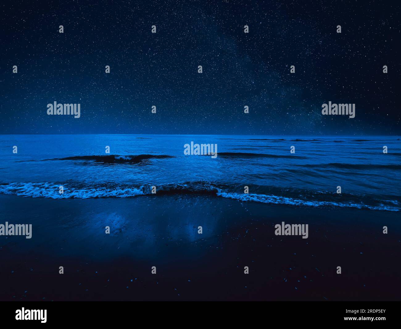 Sea waves rolling onto sandy beach under starry sky at night Stock Photo