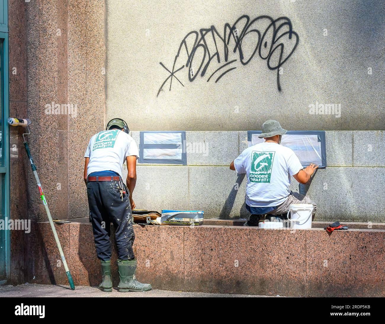 Toronto, Canada - July 19, 2023: Two men work erasing or deleting tagging graffiti from a building exterior wall in the downtwon district. Stock Photo