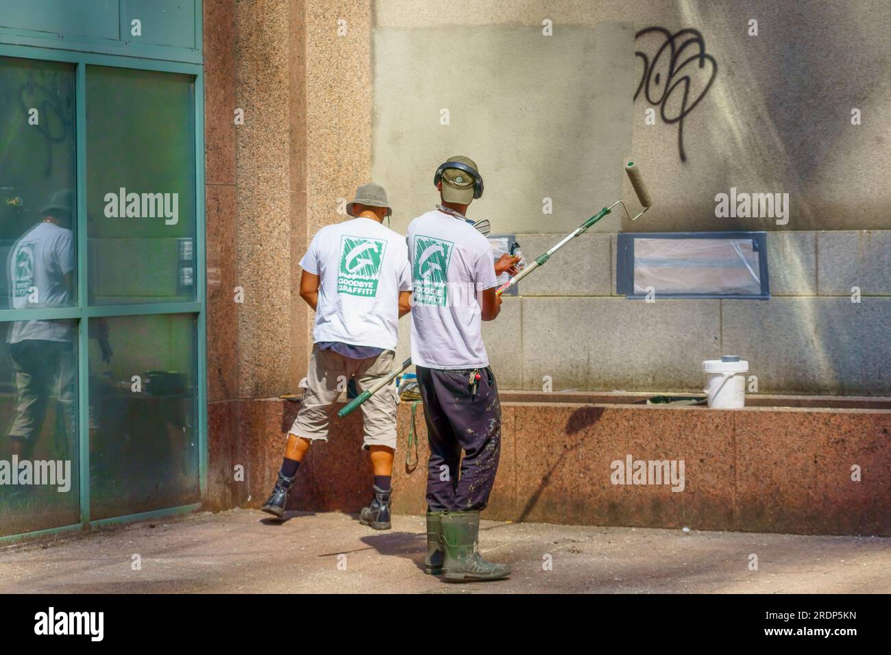 Toronto, Canada - July 19, 2023: Two men work erasing or deleting tagging graffiti from a building exterior wall in the downtwon district. Stock Photo