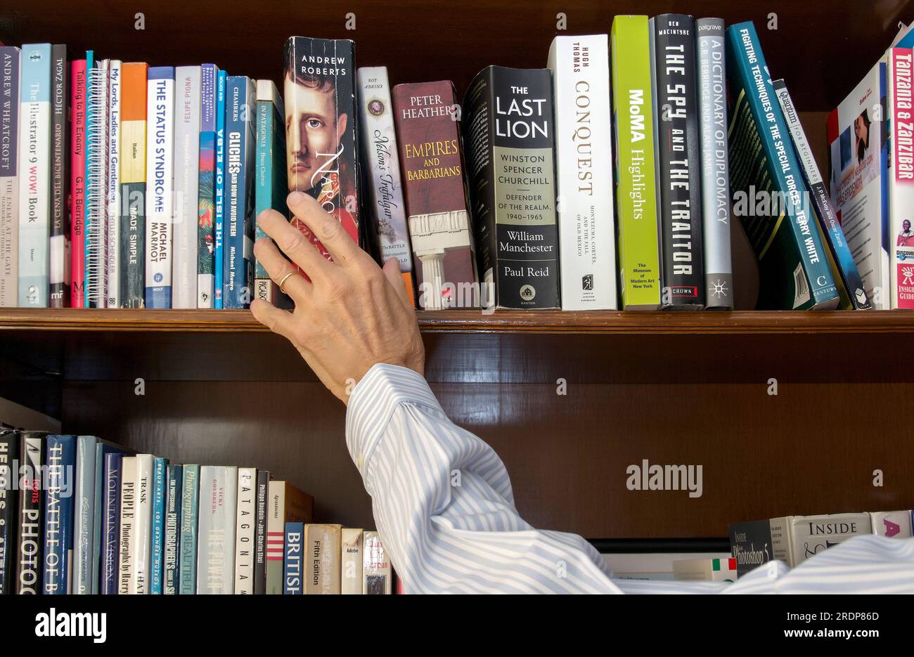 Hand reaching up for a book on library shelf Stock Photo