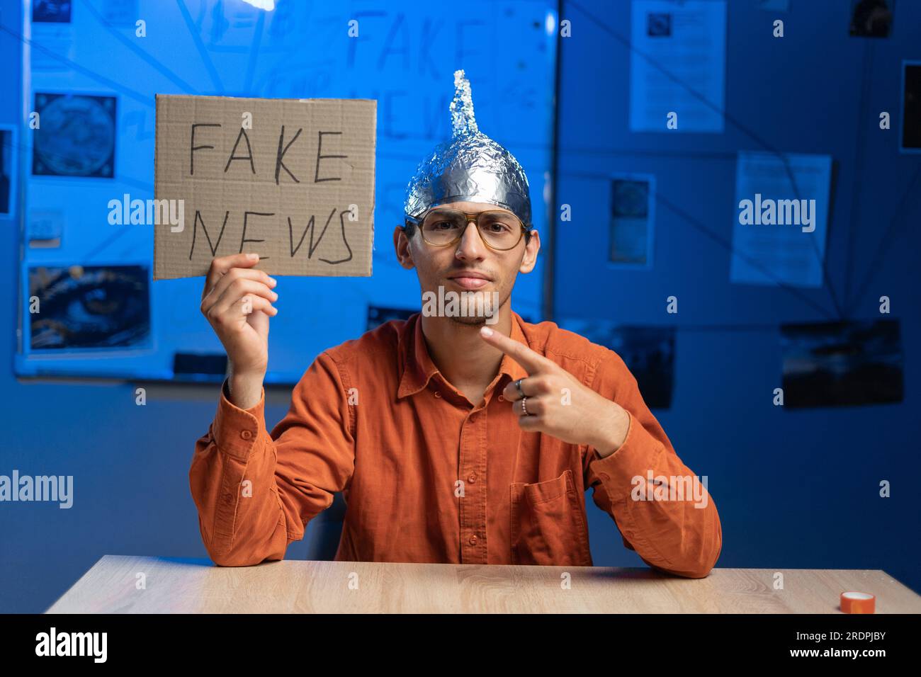 Male conspiracy theorist in a protective foil cap and glasses debunks myths holding poster fake news. Conspiracy theory concept. The schizophrenic Stock Photo
