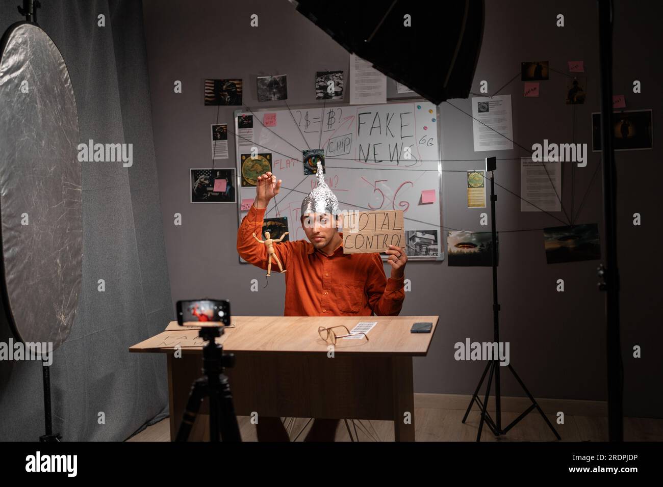 Strange young man in tinfoil hat recording video or live streaming using phone in home studio. Fake news conspiracy theories Stock Photo