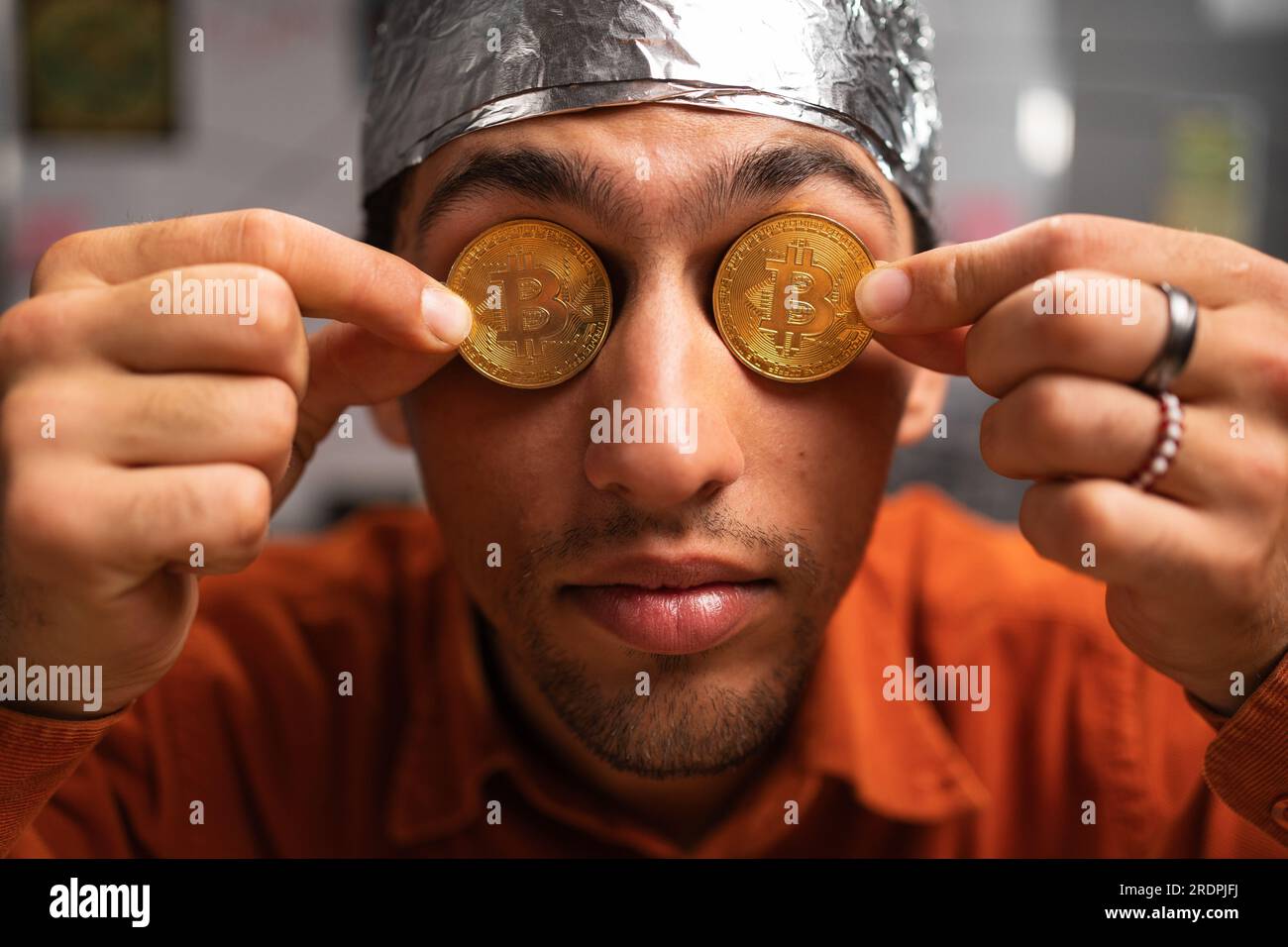 close-up a conspiracy theorist in a protective foil hat with bitcoin coins in his eyes raised his finger up on the board.Conspiracy theory concept of Stock Photo