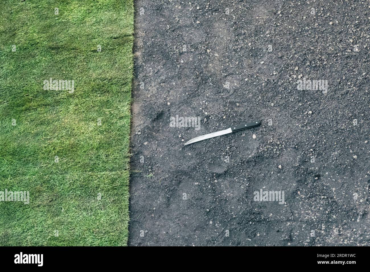 A long bladed knife lies on the ground by some newly laid turf in a small garden in the UK Stock Photo