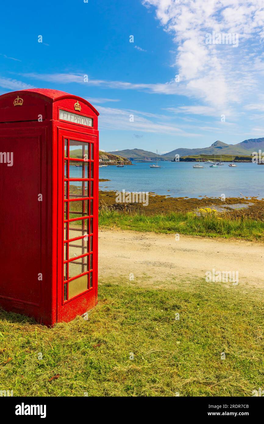 Portrait of a red, old fashioned telephone box overlooking yachts in the bay on the Isle of Canna, Small Isles, Scotland.  Copy Space, vertical. Stock Photo