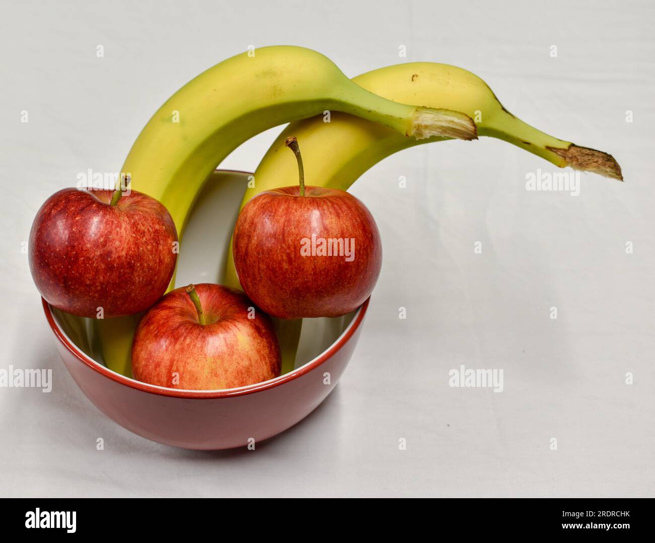 A red and white bowl containing three red apples and two bananas. Stock Photo