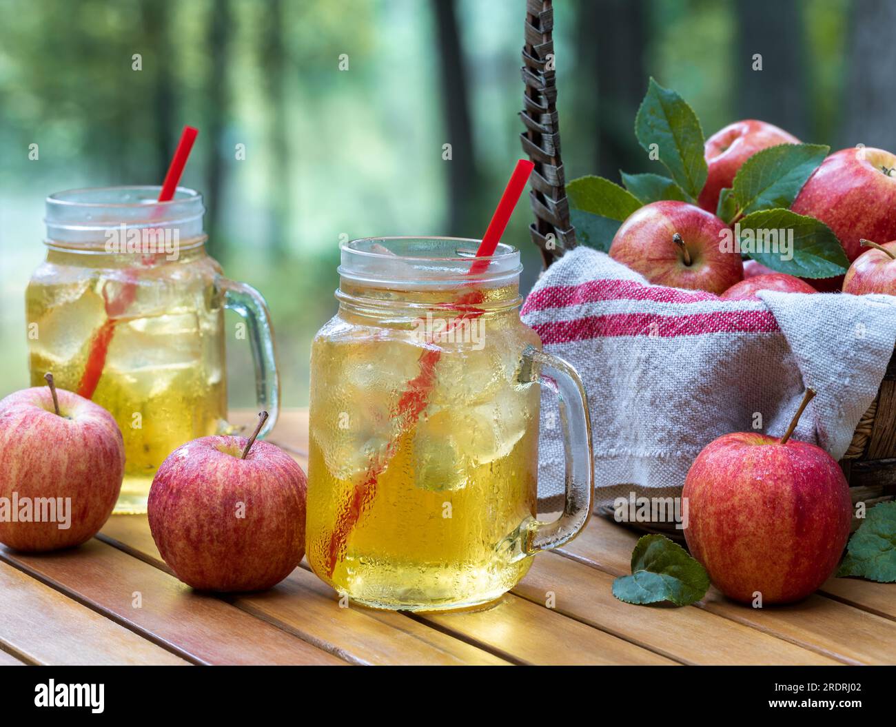 Cold apple juice in glasses with fresh apples outdoors on patio tabe with nature background Stock Photo