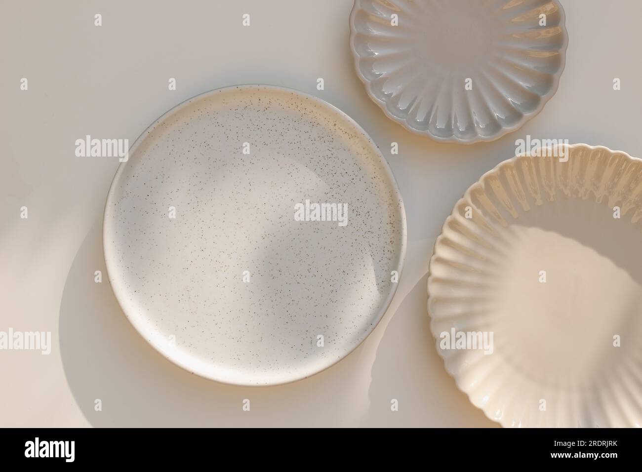 Three different size stoneware plates on beige table background. Flat