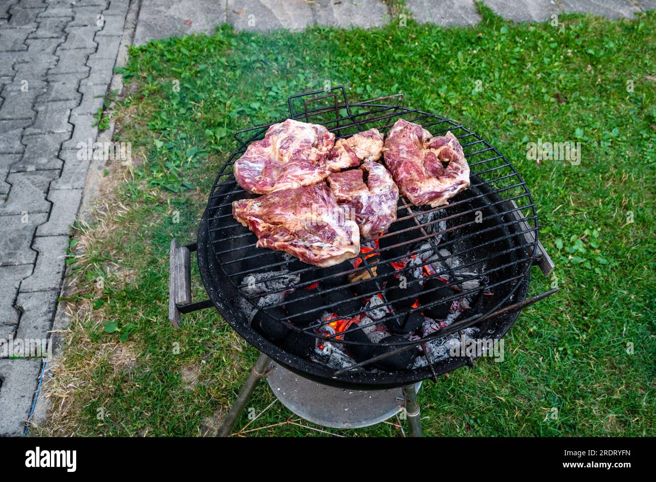 Old black outdoor grill with sliced marinated pork steak in garden. Stock Photo