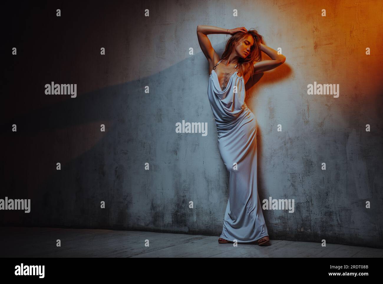 Young woman in white dress posing on wall background, tattoo on body Stock Photo
