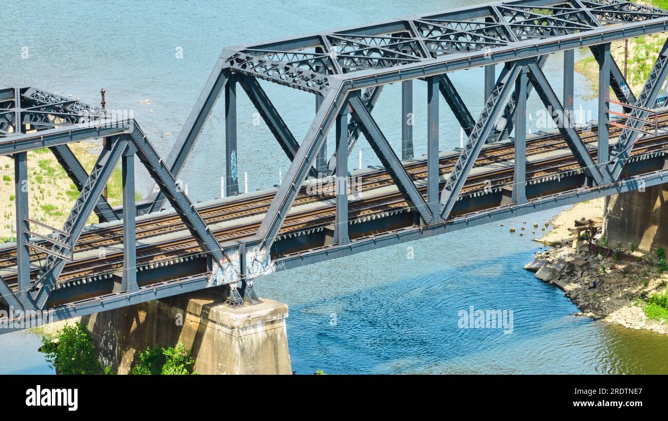 Close up of train tracks on truss train bridge over flowing river with rippled surface aerial Stock Photo