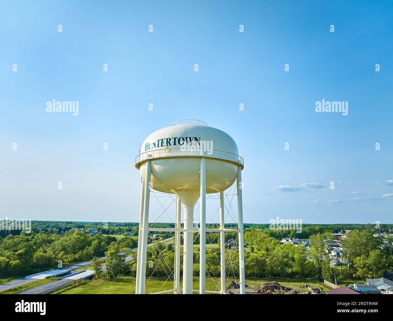 Aerial white Huntertown water tower with distant green trees and blue