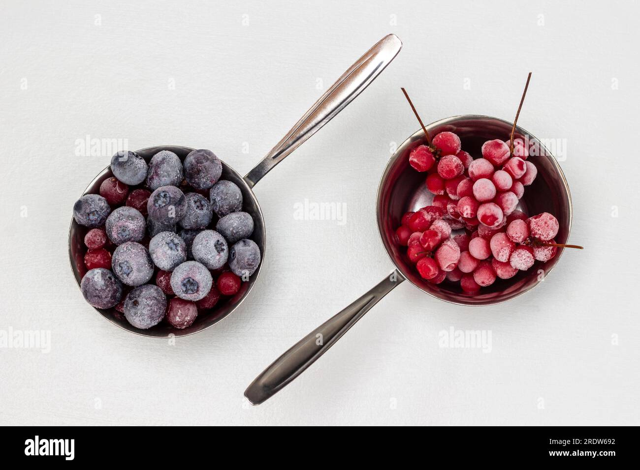 Frozen blueberries and bunches of red berries in metal bowls. Flat lay