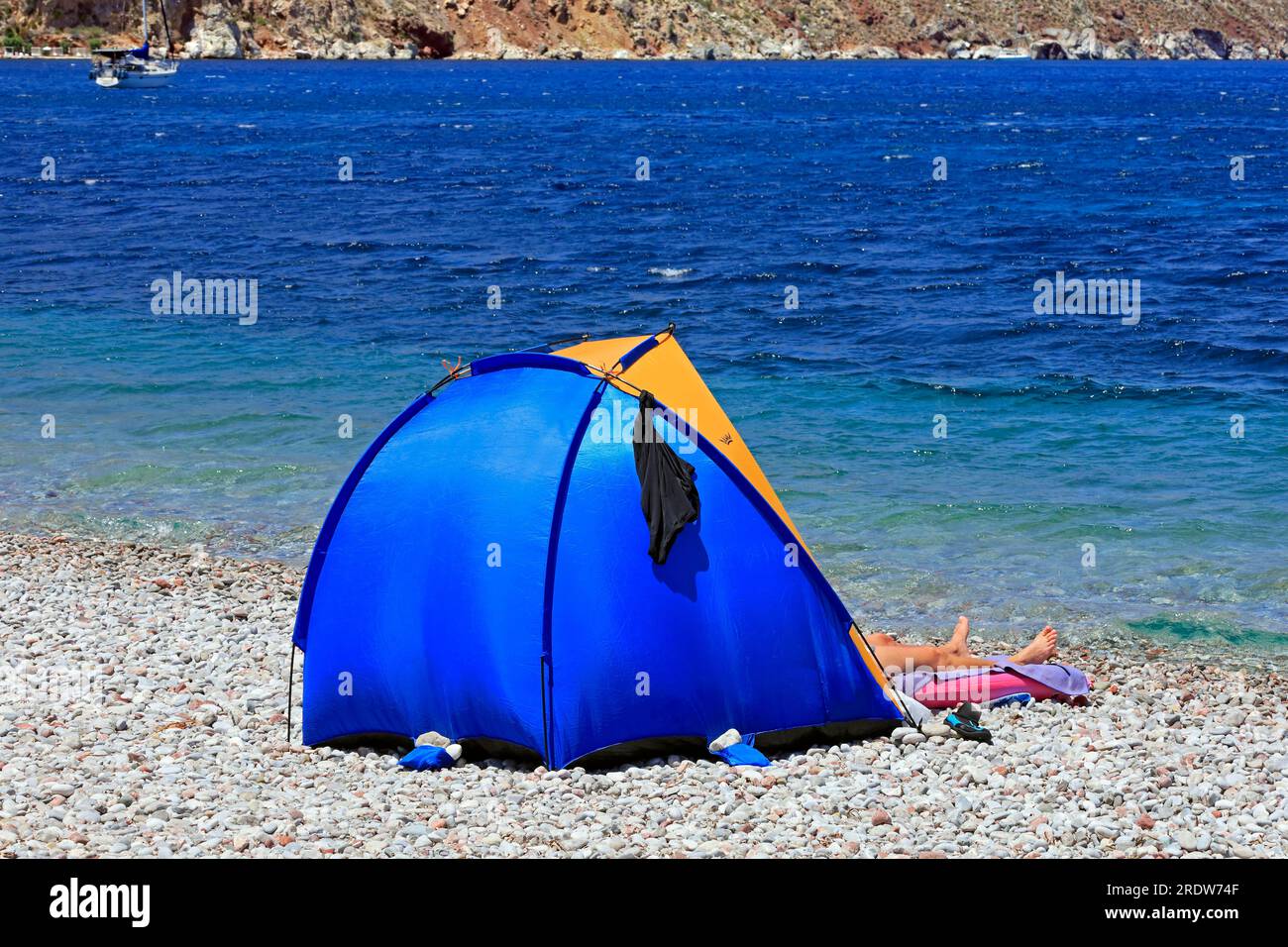 A pair of legs sticking out of a small popup sunshade tent on a stony