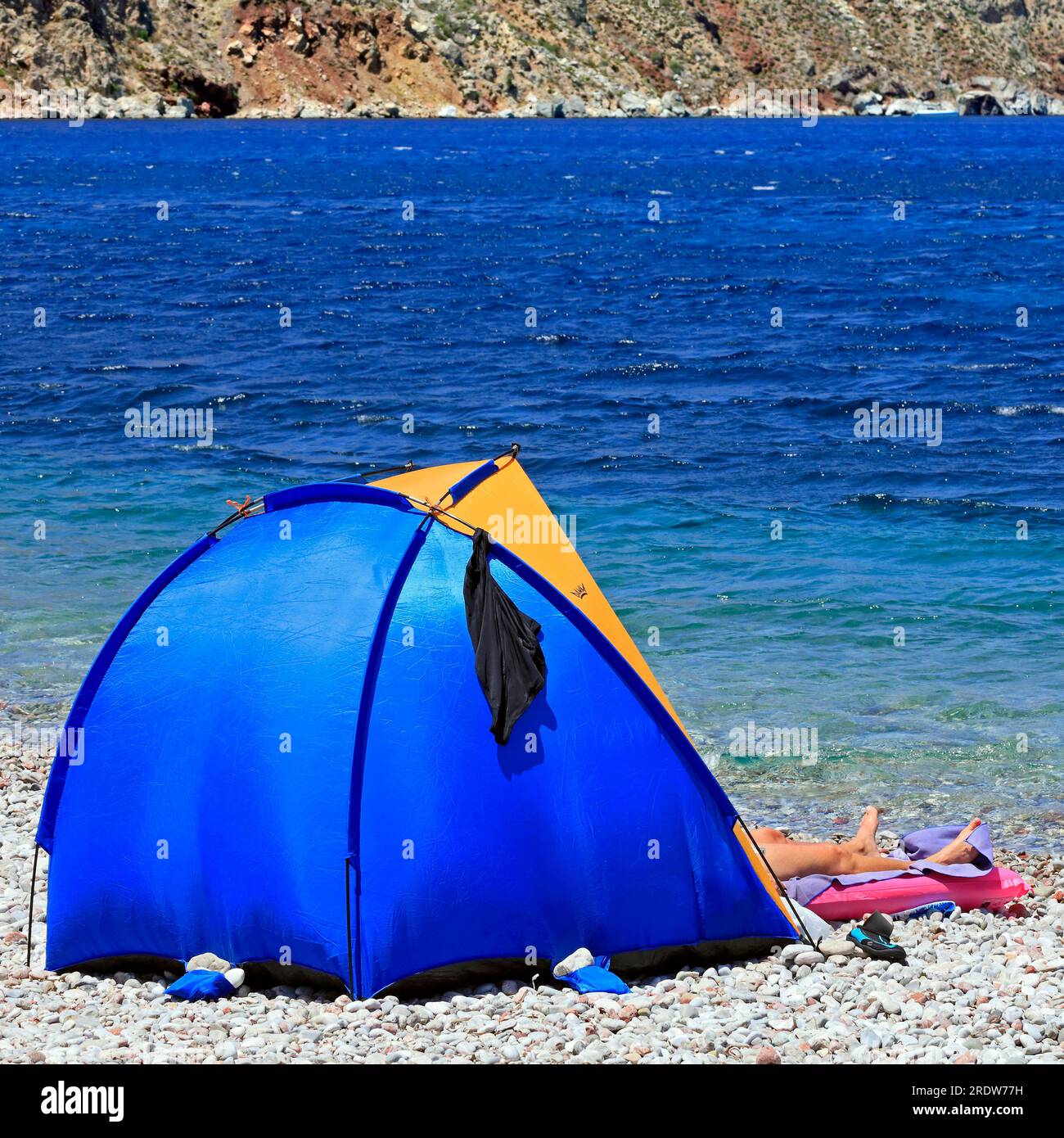 A pair of legs sticking out of a small popup sunshade tent on a stony