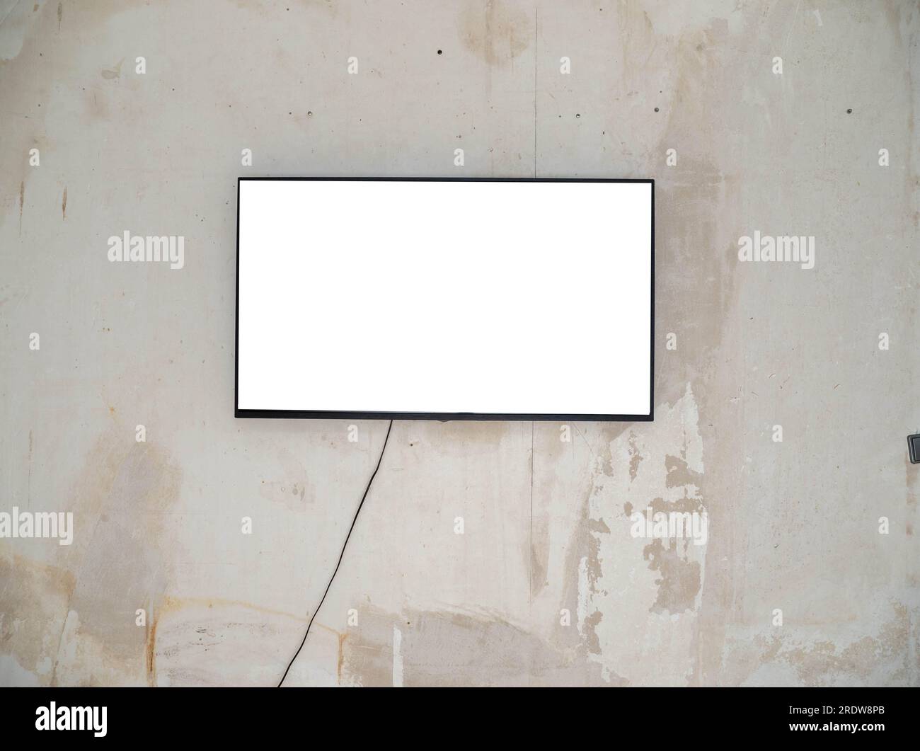 A wide white screen plasma TV in a black frame hangs on an old concrete wall. TV on a concrete wall. Stock Photo