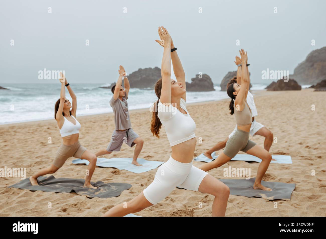 Healthy balance lifestyle. Yoga class at ocean beach in the morning doing Warrior poses with calm relax emotions Stock Photo