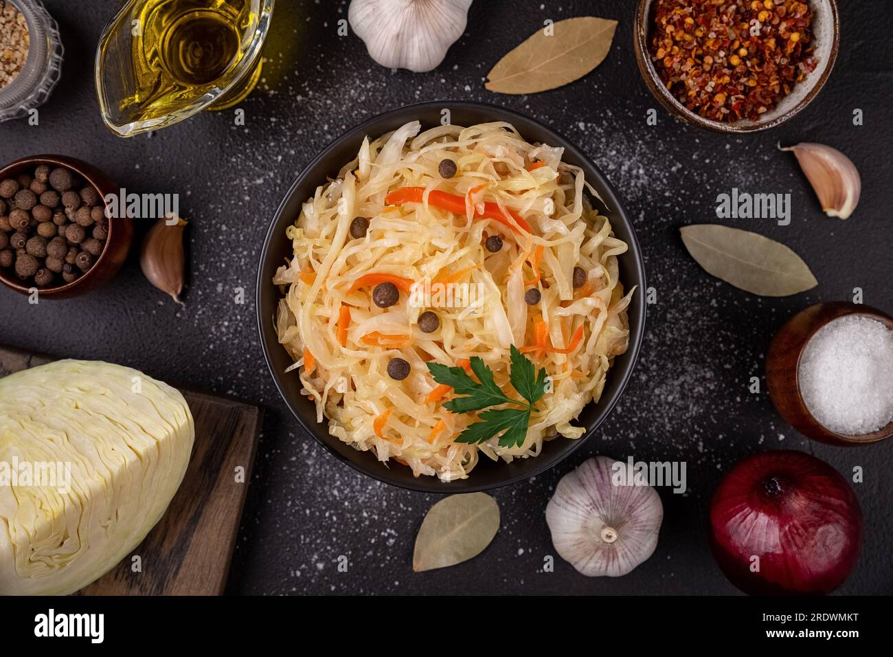 Black bowl with sour sauerkraut decorated parsley and pepper on dark background flat lay with ingredients fresh cabbage, oil, garlic Stock Photo
