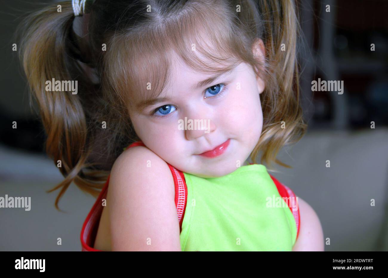 Little girl hides her chin on her shoulder and looks shyly at the