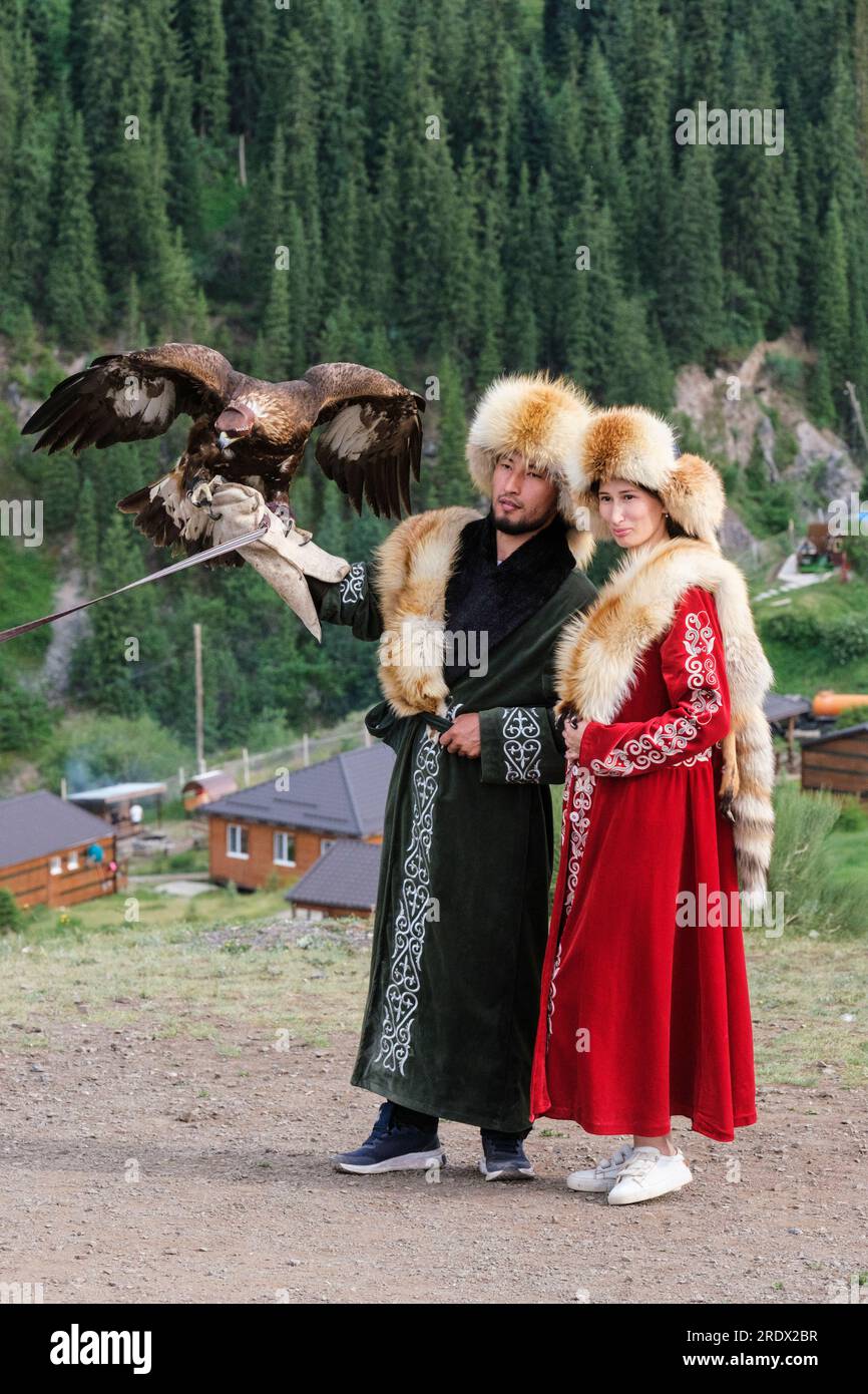 Kazakhstan, Kolsay Lakes National Park. Couple Posing for Photo in Traditional Costume with Hooded Falcon. Stock Photo