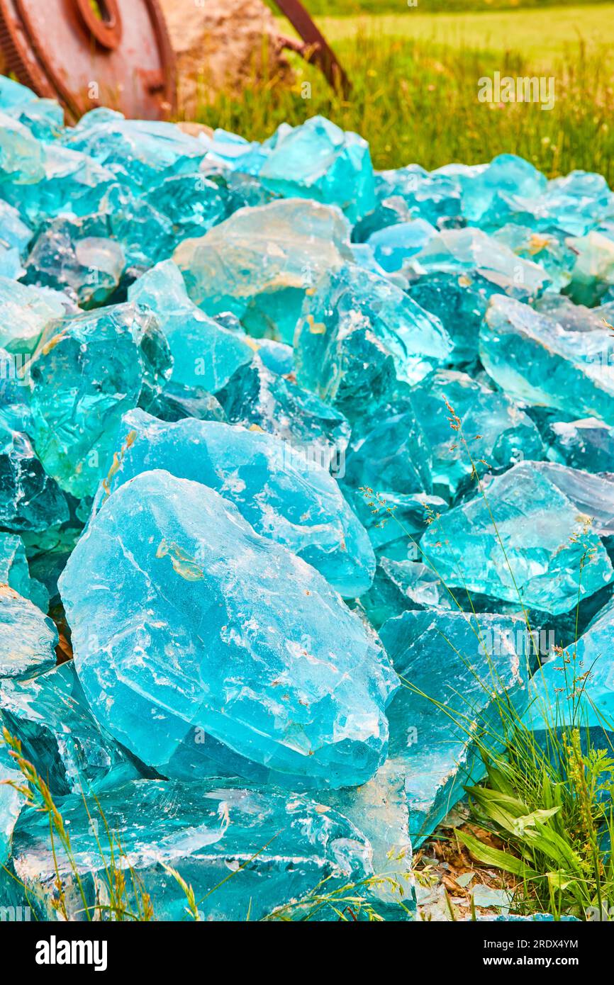 Pile of cloudy blue glass crystals laying in grassy field vertical