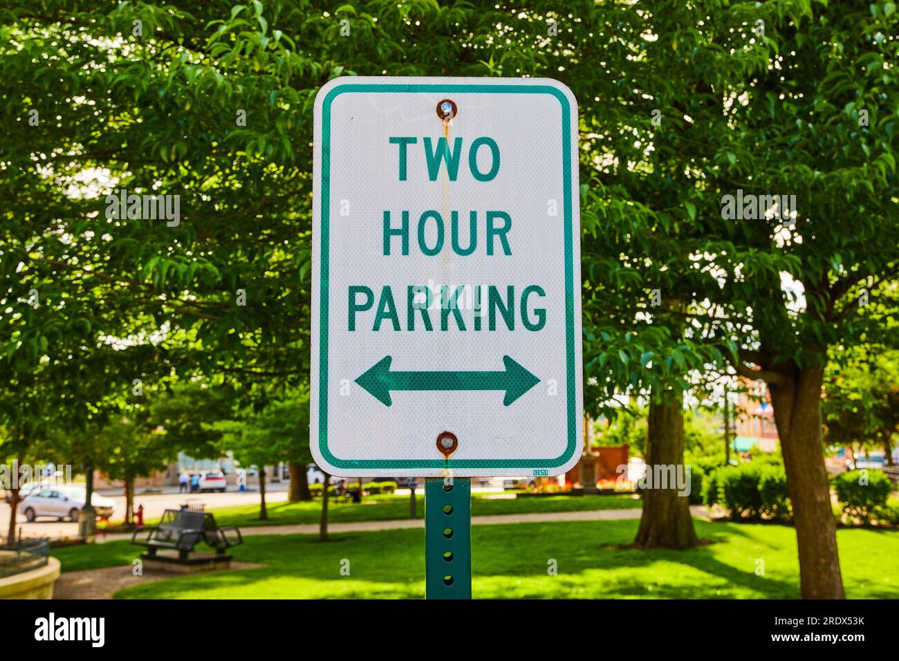 Close up of green Two Hour Parking sign in front of a park in