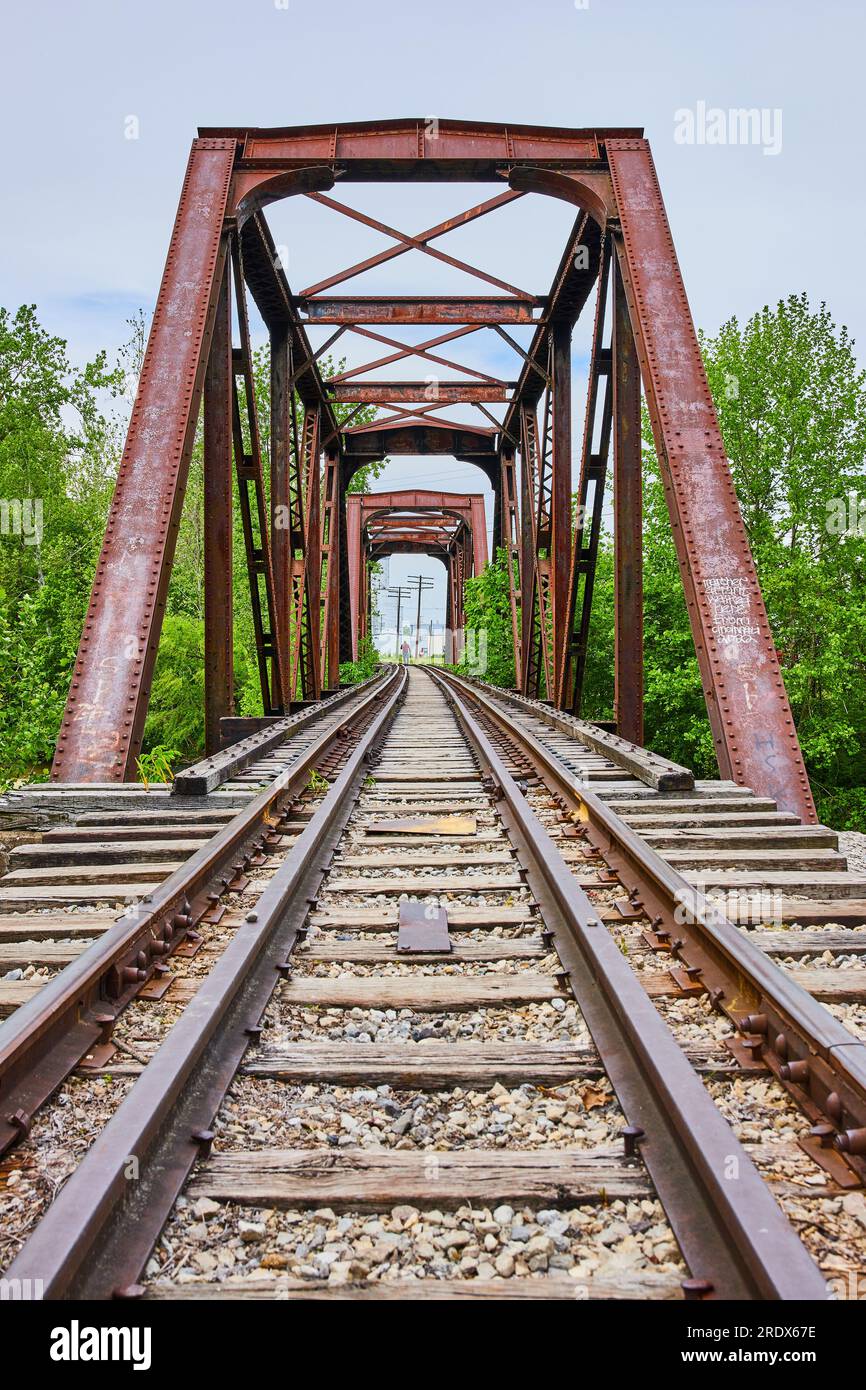 Train tracks leading to rusty iron truss railroad bridge leading