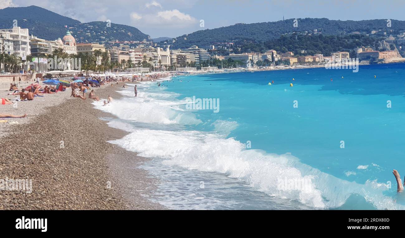 Idyllic relaxation on  beach in:  tendering waves and palm trees of Promenade de Anglais in Nice  of French Riviera.   People enjoy sun and summer and Stock Photo