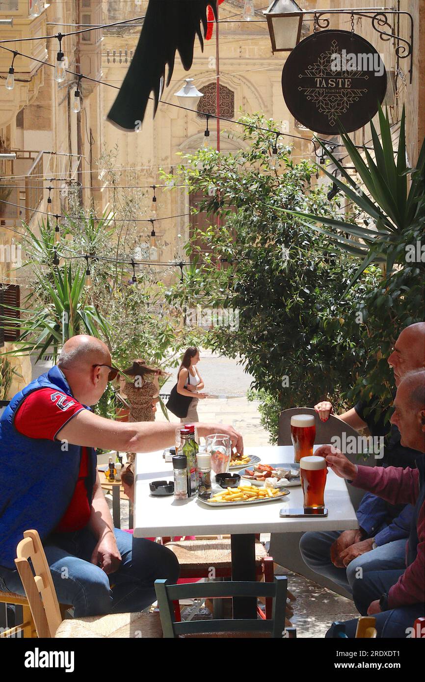 Three middle aged men enjoy a lunchtime pint to wash down their side orders of chips, dining at Taste Restaurant, St Lucy Street, Valletta, Malta. Stock Photo