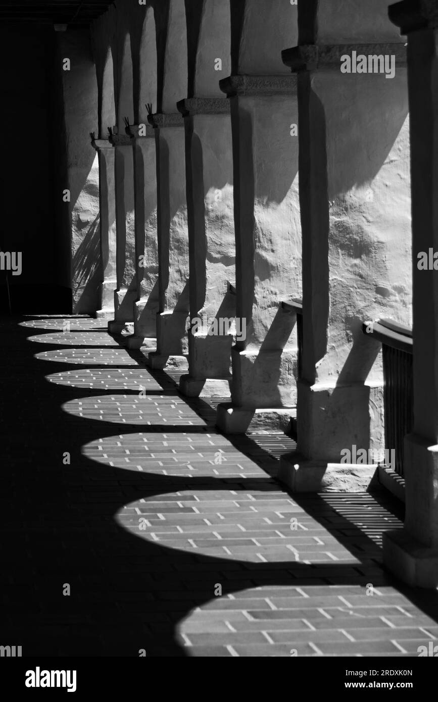 A black and white image of a long line of arches that create rich contrasts and dark shadows. Stock Photo