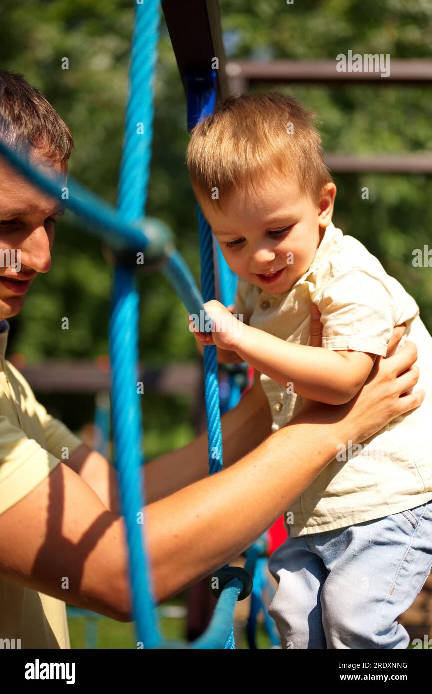 Little toddler playing on the playground with a help of his father Stock Photo