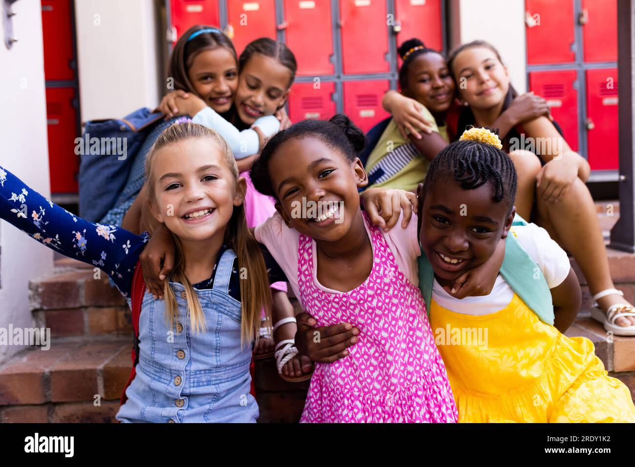 Portrait of diverse happy schoolgirls embracing in elementary school cloakroom Stock Photo