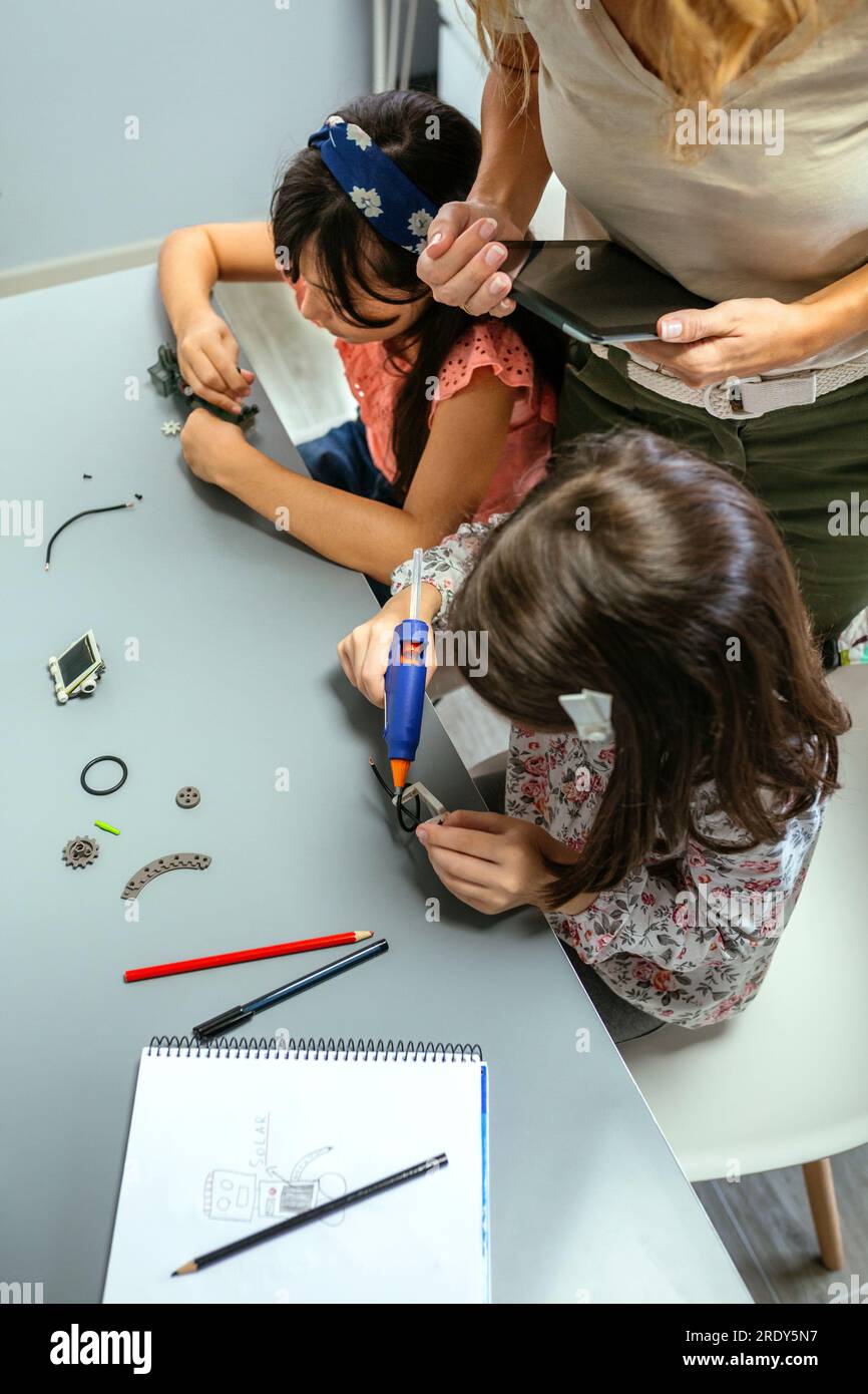 Student Using A Machine Students working with machine pieces next to teacher in robotics class ...