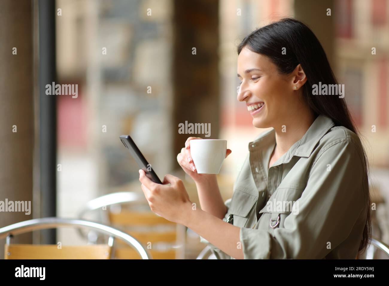 Happy woman drinks coffee in a bar terrace using smart phone Stock Photo