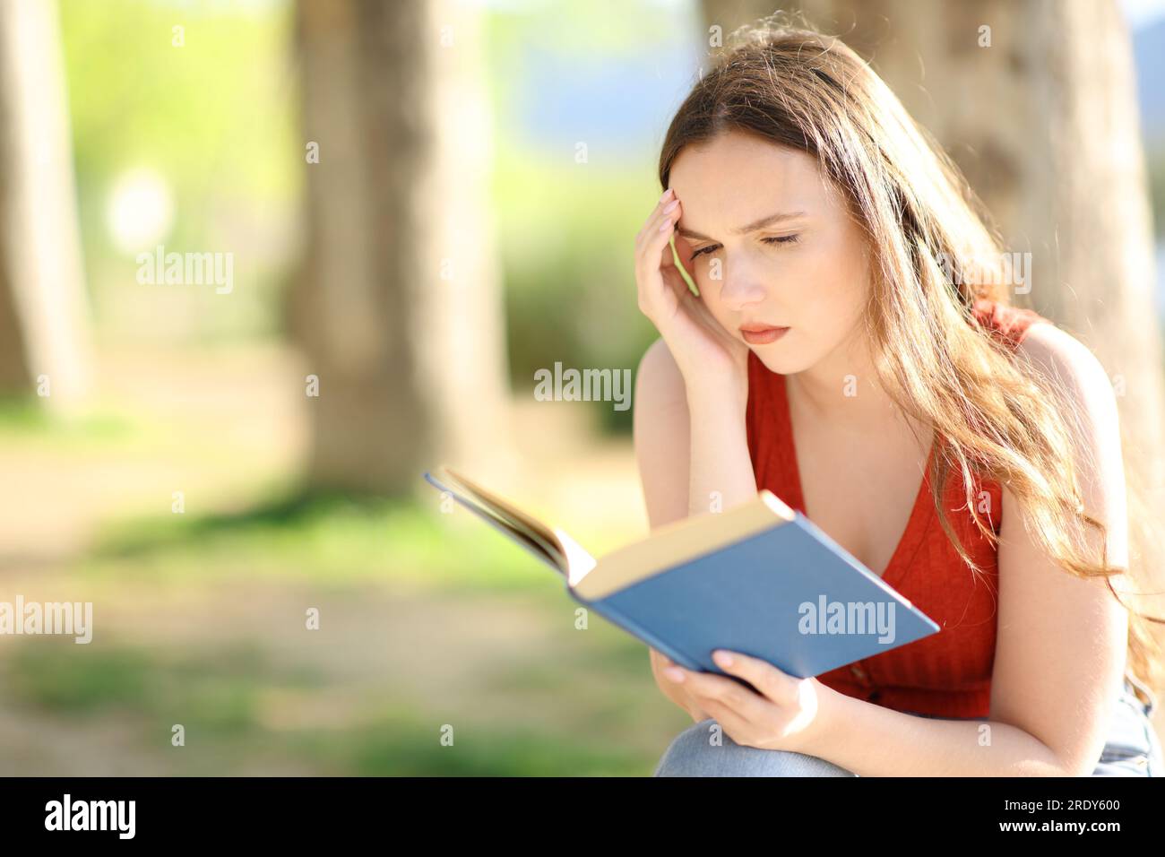 Worried woman reading a paper book sitting in nature Stock Photo