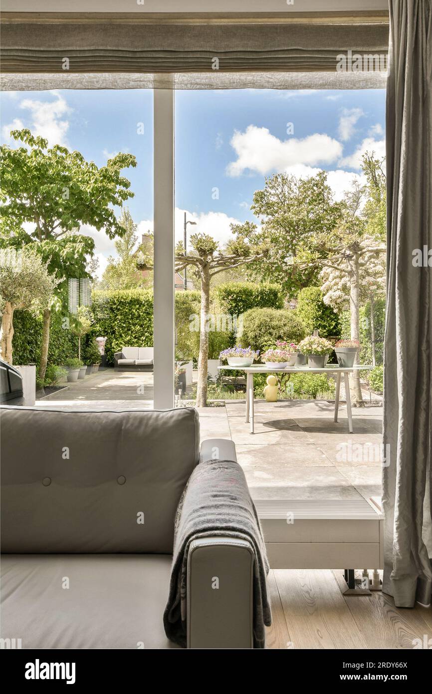 a living room with a couch and large window looking out onto the backyard garden, which has been used for many years Stock Photo