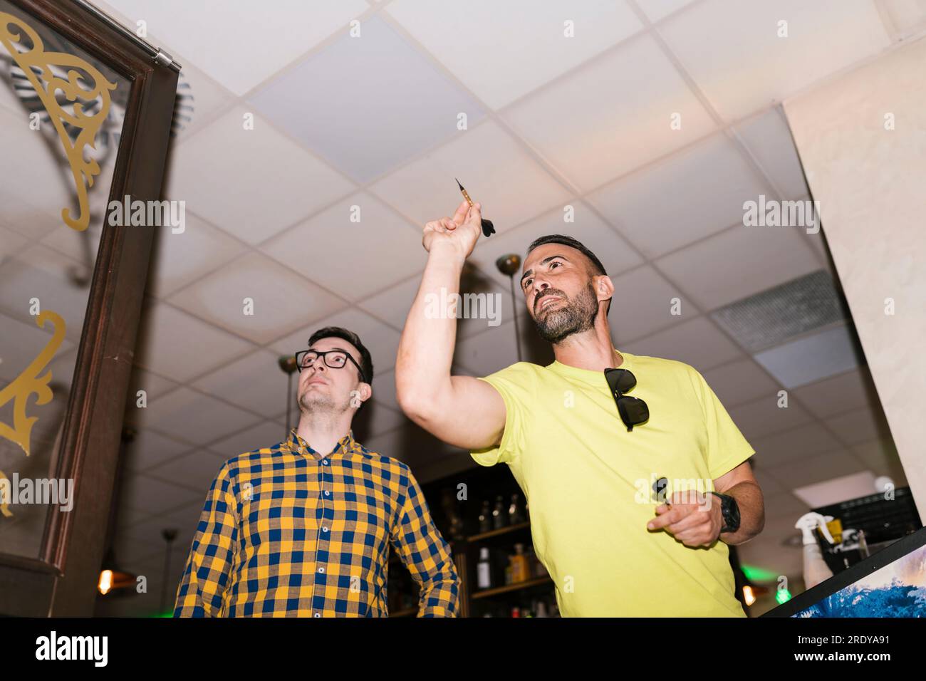 Man aiming dart on target standing next to friend at bar Stock Photo