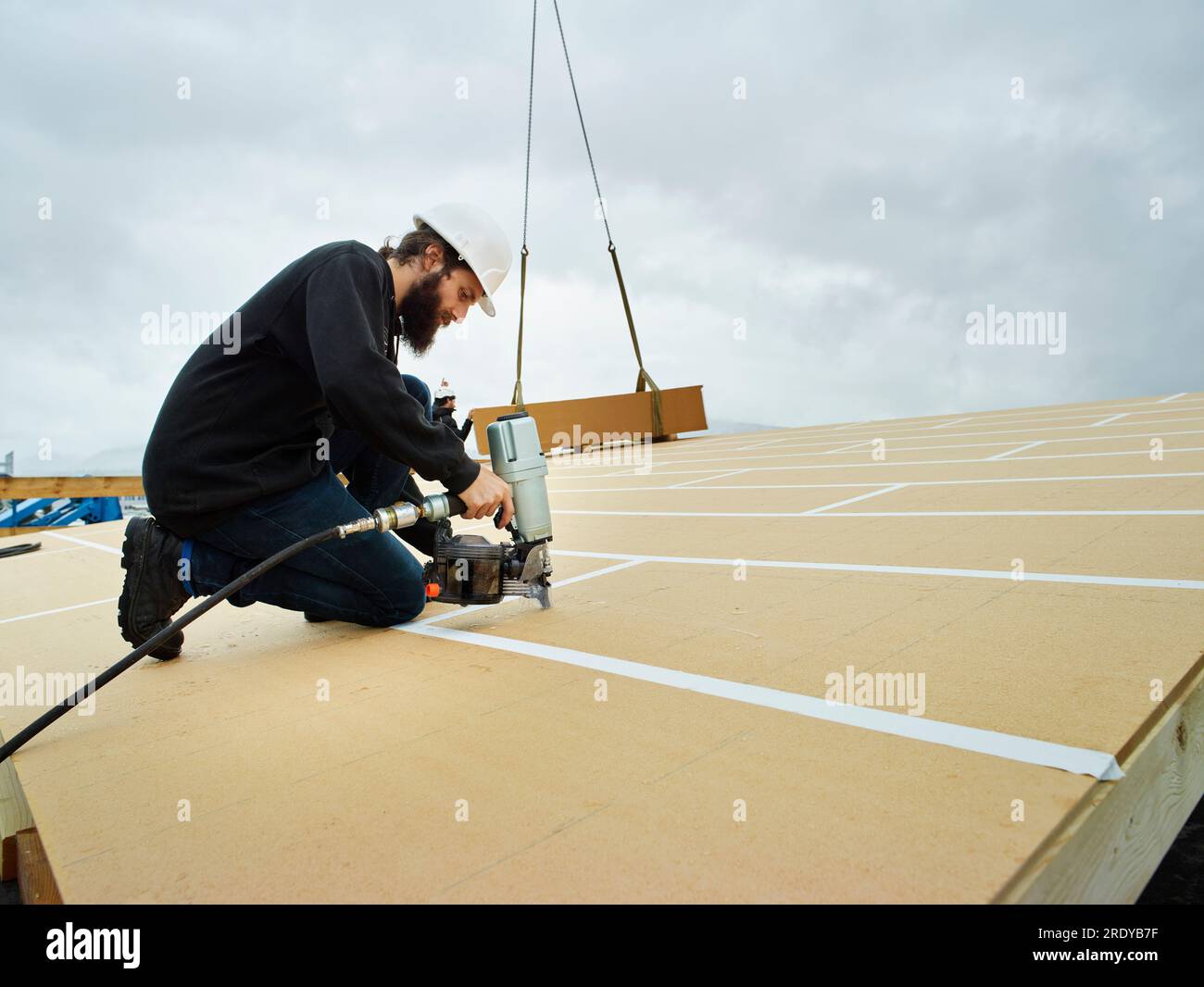 Carpenter using nail tool on wooden rooftop Stock Photo