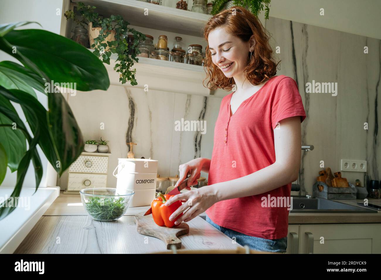 Happy young woman cutting red bell pepper in kitchen at home Stock Photo