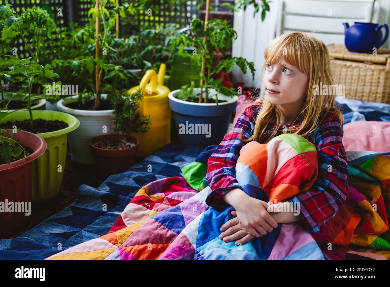Contemplative girl wrapped in quilted blanket sitting in balcony Stock Photo
