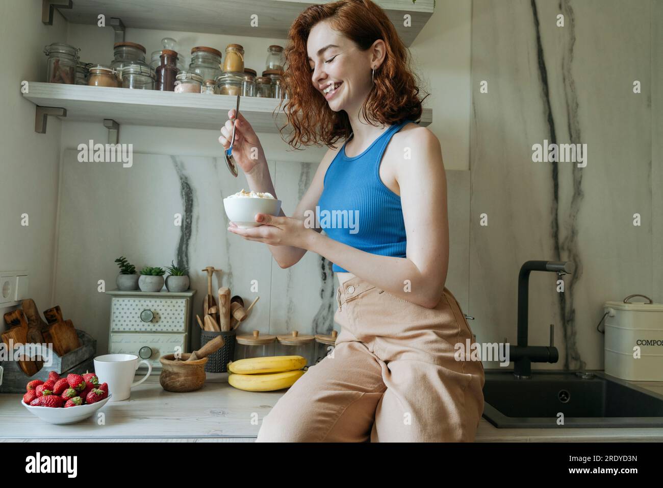 Happy young woman having breakfast in kitchen at home Stock Photo