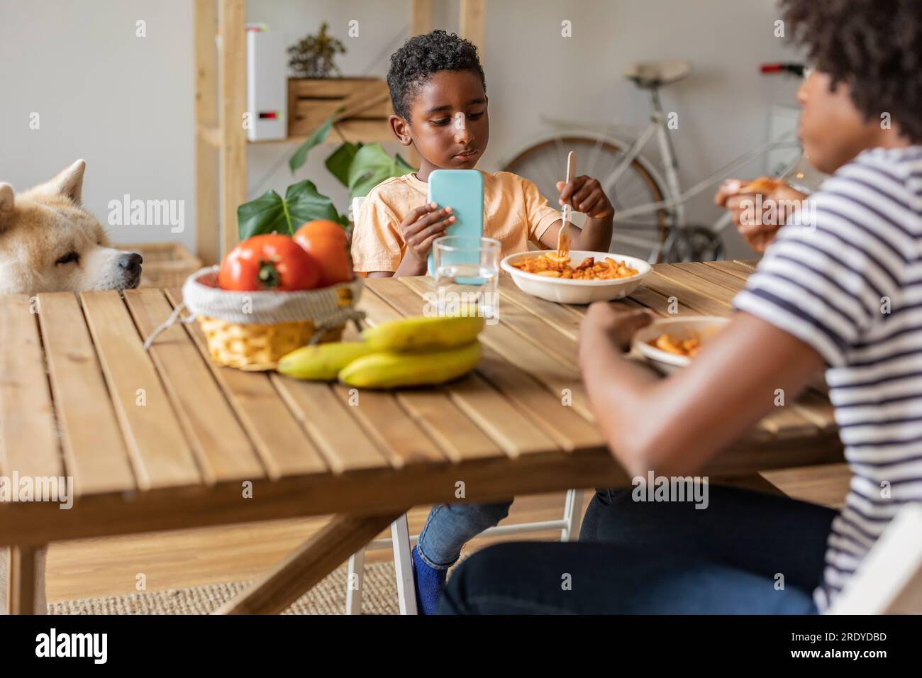 Young woman with boy holding smart phone and having meal at home Stock Photo