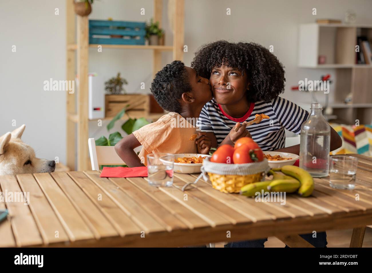 Boy kissing mother on cheek and having meal together at home Stock Photo